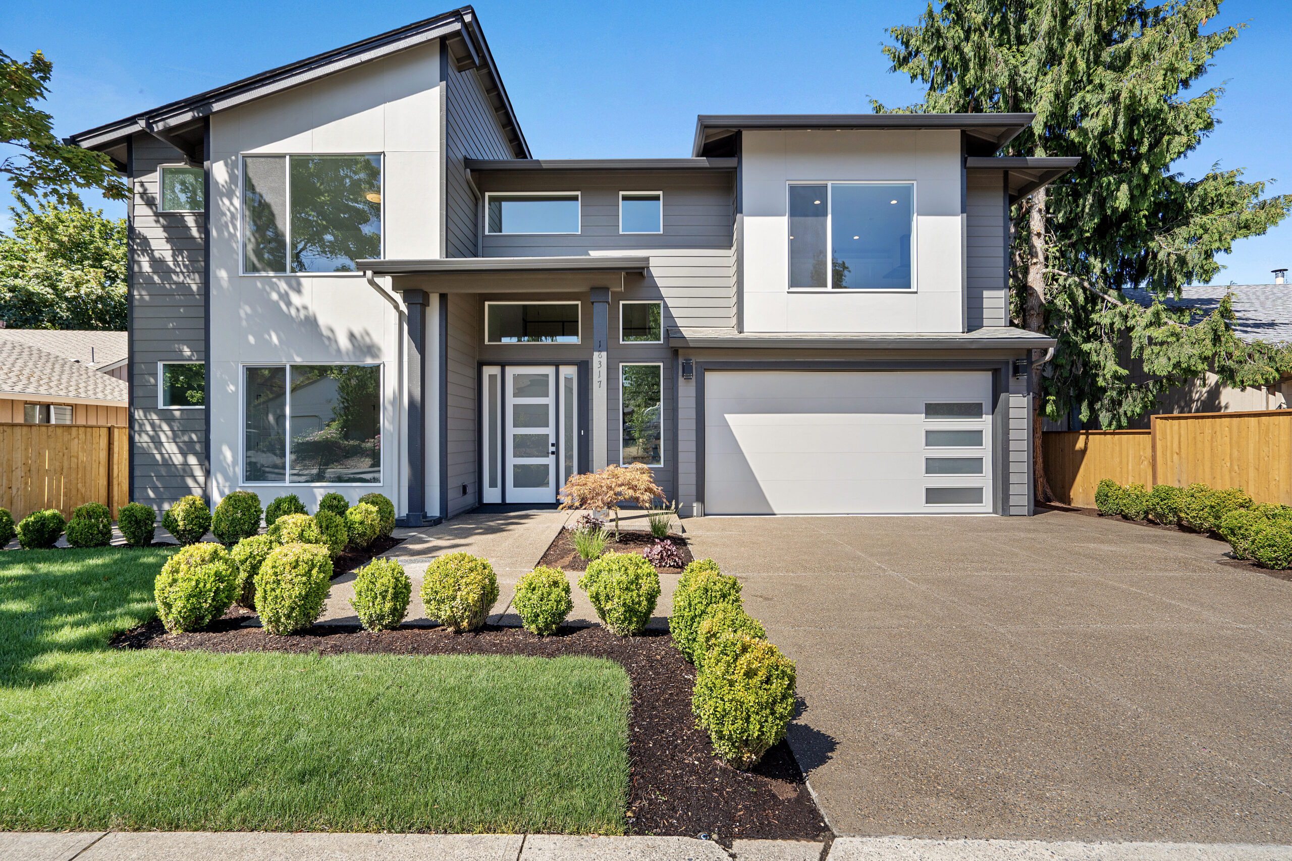 Modern two-story home with large windows and landscaped front yard under a blue sky.