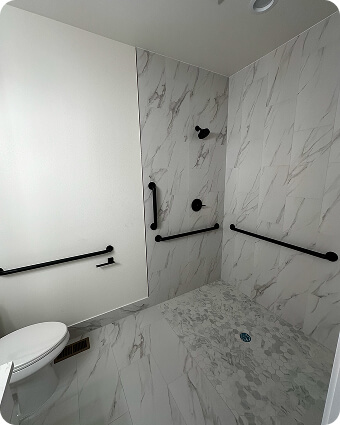Accessible bathroom with tiled walk-in shower and black grab bars.